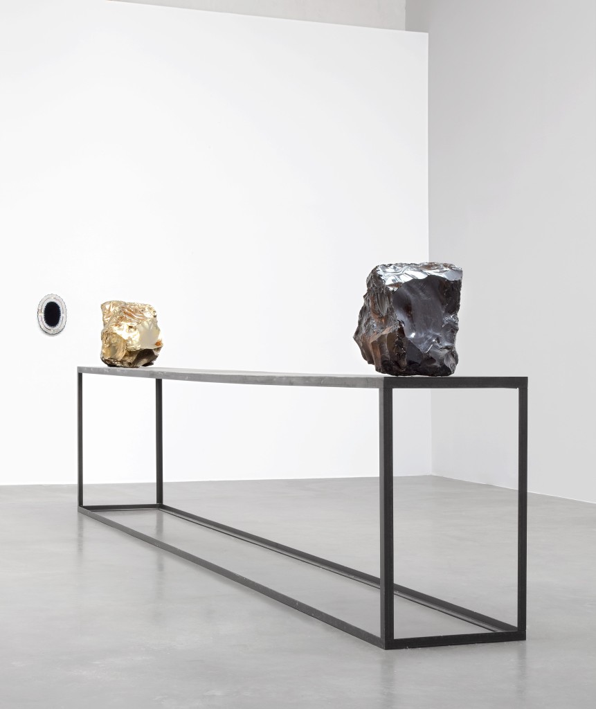 Jimmie Durham, Upon reflection, I was no longer sure of my position, 2009. Obsidian, German silver (copper, zinc, and nickel), steel table, obsidian mirror with colored tin frame. Mirror: 13 ½ × 10 × ¾ in. (34 × 25 × 2 cm); table: 39 ½ × 197 × 23 ½ in. (100 × 500 x 60 cm); obsidian: 18 ½ in. (47 cm) diameter; German silver: 17 ¾ in. (45 cm) diameter. Hammer Museum, Los Angeles. Purchase. Image courtesy of kurimanzutto, Mexico City. 